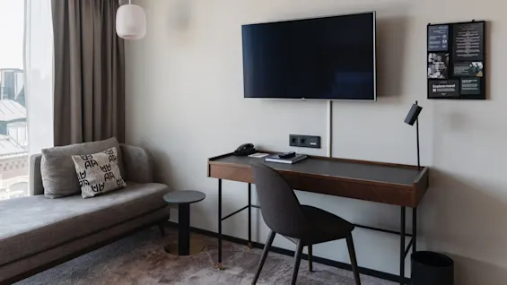 Modernt rum med en väggmonterad TV, soffa, skrivbord och hänglampa, ger en inbodd känsla.