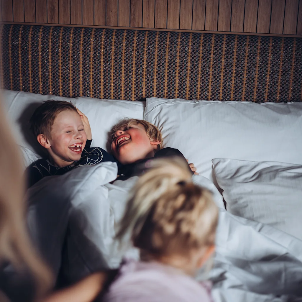 Barn som nyter et øyeblikk med latter og lek i en komfortabel seng, med ett barn i forgrunnen.