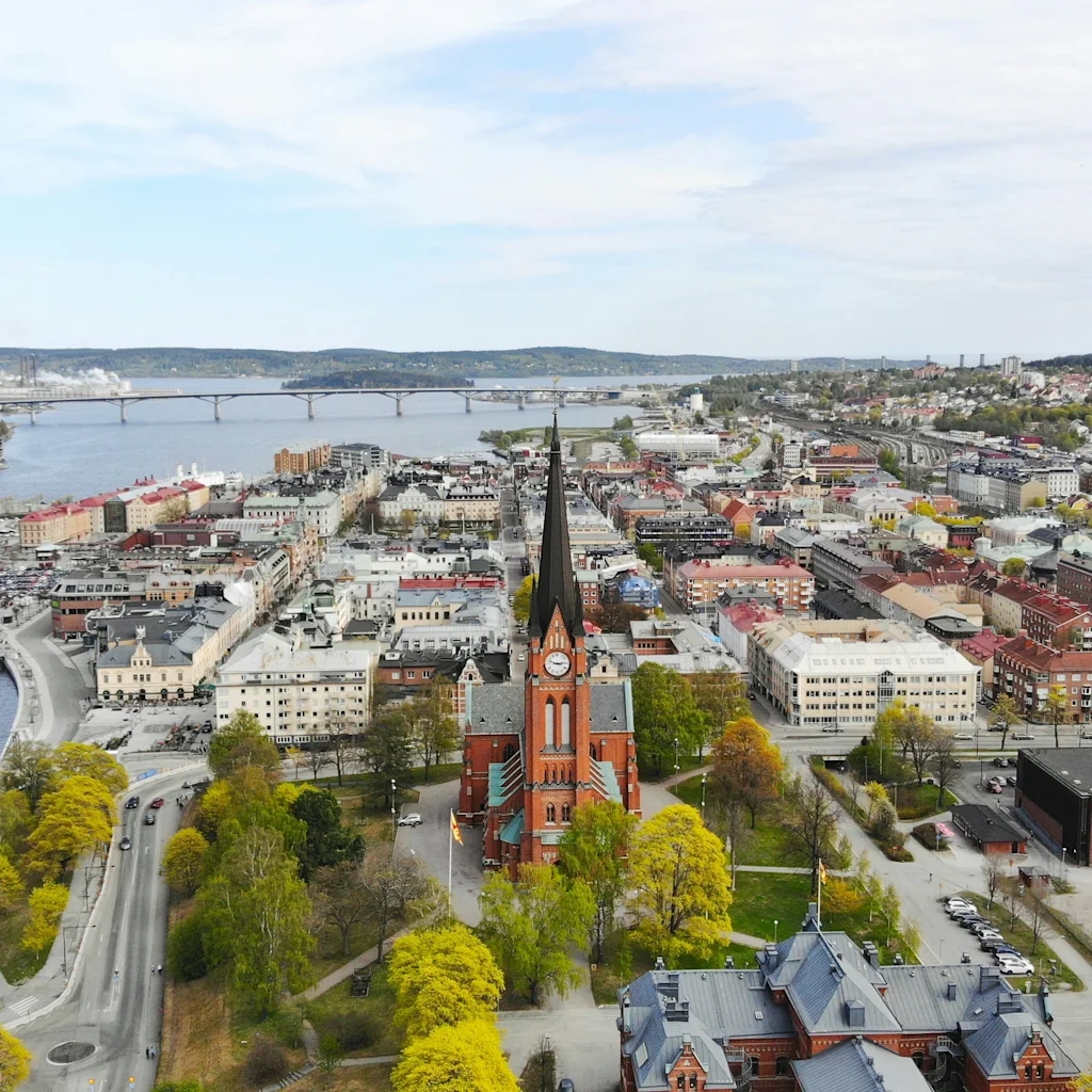 Aerial view of Sundsvall city with a prominent church, river, bridges, and urban landscape under a cloudy sky.
