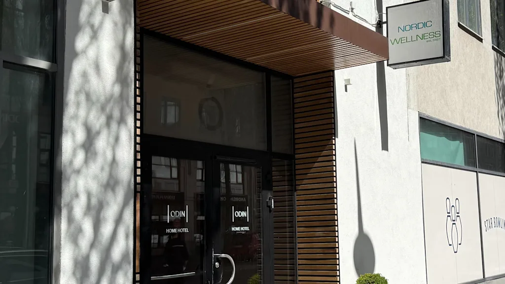 Building entrance with glass doors and a wooden canopy. Signs for HOME HOTEL and WELLNESS are visible, plus a STAR BOWLI graphic.