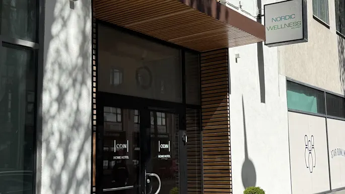 Bygningsinngang med glassdører og et tretak. Skilt for HOME HOTEL og WELLNESS er synlige, pluss en STAR BOWLI grafikk.