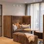 Hyggelig siddeområde med høje, polstrede bænke og runde borde, omringet af blød belysning og gulv-til-loft gardiner. I nærheden en glasdør med et synligt grønt udgangsskilt.