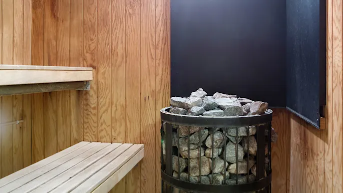 Et sauna-interiør med trebenker og en varmeovn fylt med steiner.