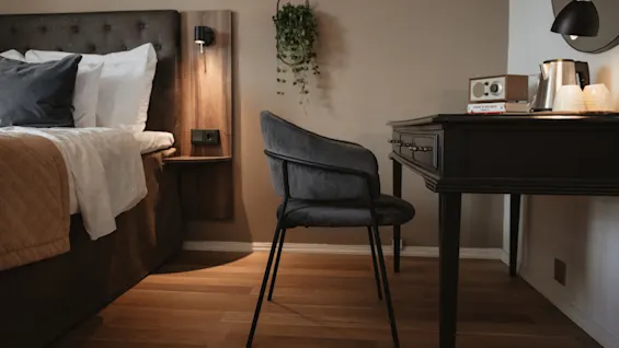Mukava hotellihuone, jossa on sänky, työpöytä vedenkeittimellä ja radiolla sekä tyylikäs tuoli.