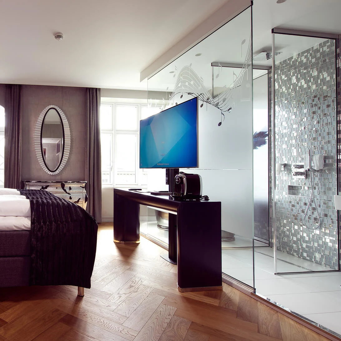 Bed with plush pillows against a swan mural; modern room features wood flooring, frosted glass shower, TV, and mirrored cabinet under soft lighting.