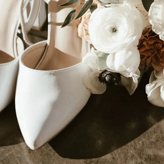Hvite elegante sko ved siden av en bukett med hvite blomster, som antyder en spesiell anledning eller feiring.