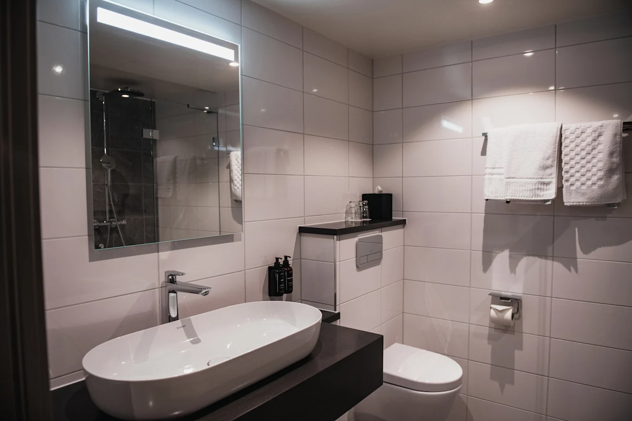 Et rent og moderne bad med et stort speil, en stilig vask og friske håndklær, som skaper et innbydende rom.