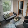 Relaxation area with a view of trees, sofa, armchairs, and a coffee table. Sauna entrance. Sign: Regler for bruk av badstuen.