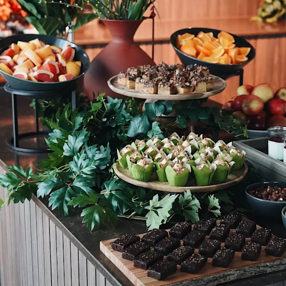 Ulike desserter og frukt er elegant vist på en buffé med grønne aksenter. Ulike bakverk, fruktskiver og glass med yoghurt skaper en fargerik, innbydende presentasjon.
