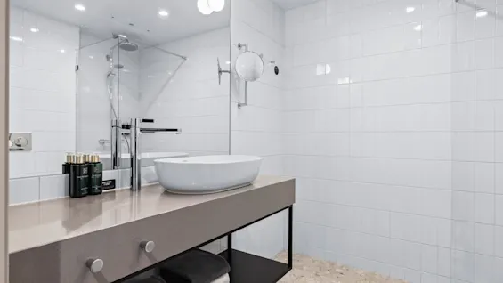 Sink resting on a countertop with towels stored underneath in a modern bathroom featuring white tiled walls and a glass shower enclosure.
