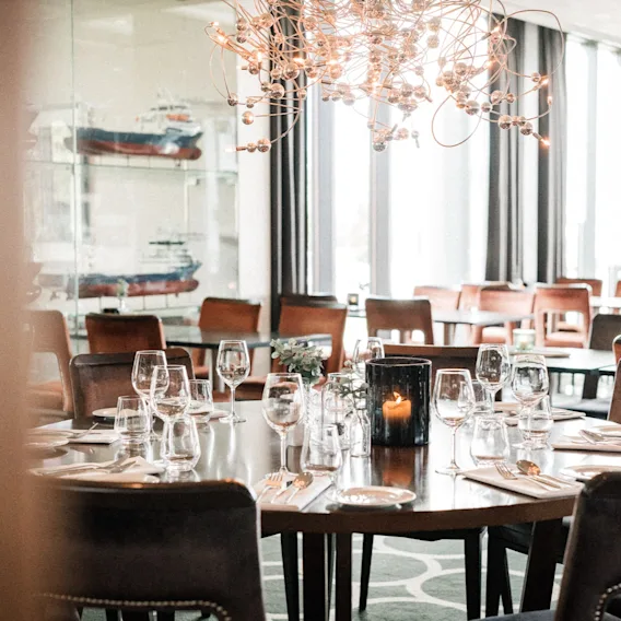 En restaurant spisesal med dekkede bord, stoler, et tent lys og dekorative skipsmodeller.