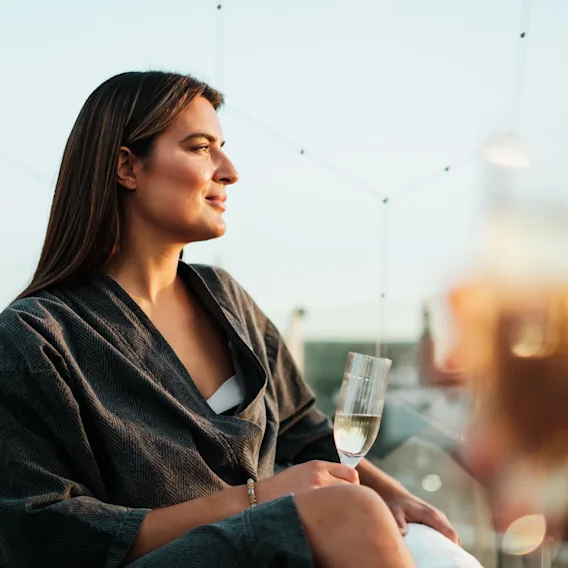 En person i morgonrock njuter av en drink på en takterrass eller balkong och tittar ut över utsikten.