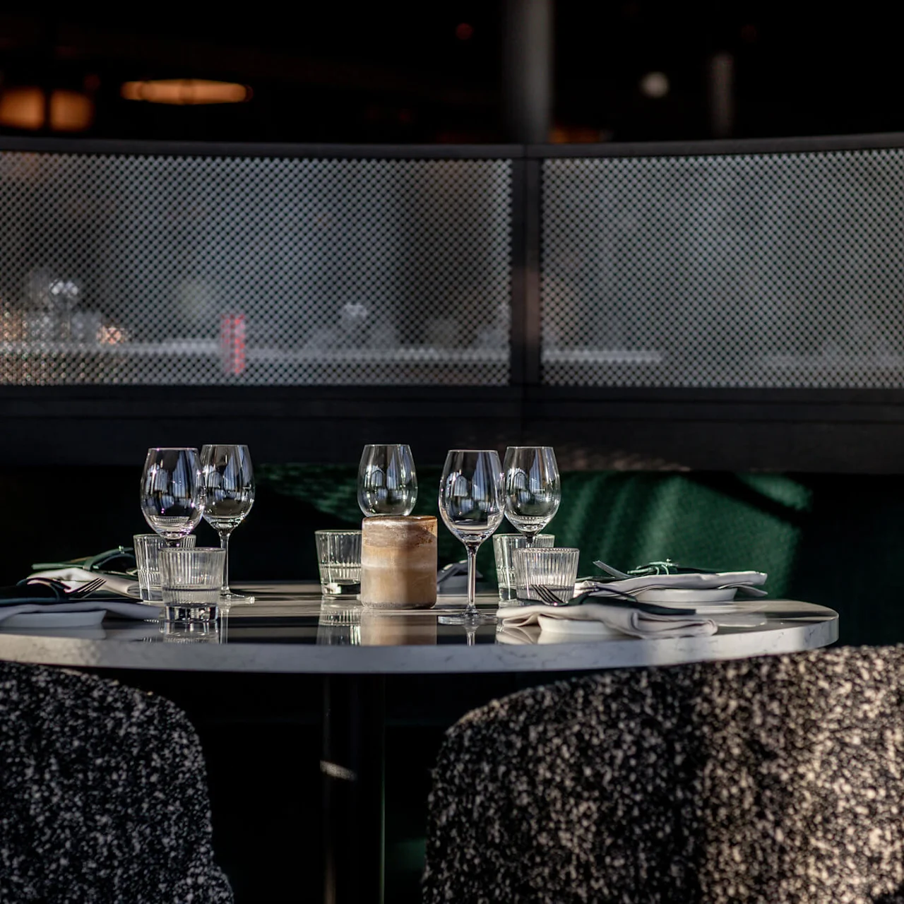 Et rundt spisebord med vinglas, servietter og bestik; omgivet af bløde stole i en svagt oplyst, hyggelig restaurantbås.
