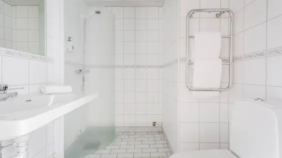 A clean, modern bathroom with white tiles, a sink, a shower with a frosted screen, a toilet, and a towel warmer.