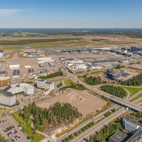 Ilmakuva vilkkaasta lentokentästä, läheisistä liikerakennuksista, monimutkaisista tieverkostoista ja rehevistä vihreistä maisemista.