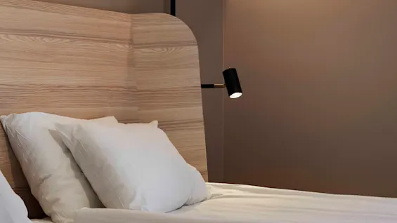 Ett mysigt hotellrum med en säng med krispiga vita sängkläder, en sänggavel i trä och varm belysning från vägglampor.