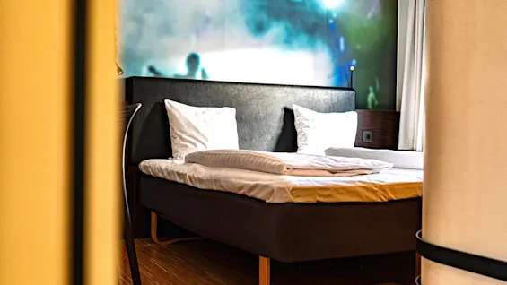 Ett modernt hotellrum med en säng och en livlig väggmålning som föreställer en konsertscen.