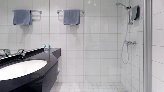 A modern bathroom with tiled walls, a glass shower, a sink, and towels hanging on a rack.