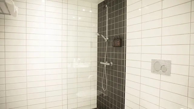En moderne dusj med et elegant dusjhode er montert på en vegg av svarte fliser, omgitt av et bad med hvite fliser. Det er en glassvegg og en dobbeltskyllingstoalett.