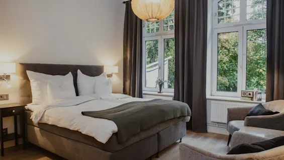 Et hyggeligt hotelværelse på Home Hotel Norre Park i Halmstad med en komfortabel seng, lænestole og vindue mod grønne områder.