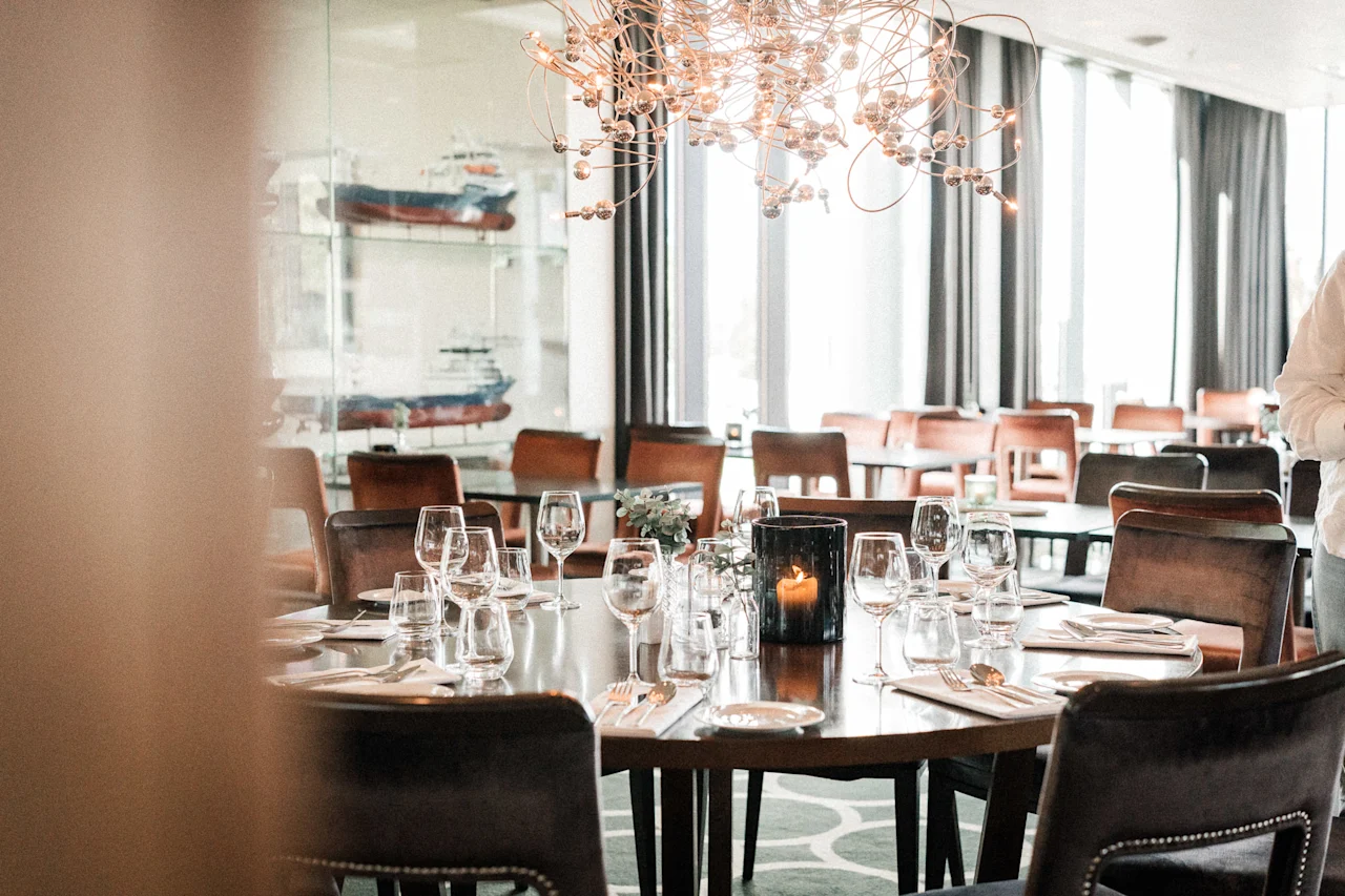 En restaurant spisesal med dekkede bord, stoler, et tent lys og dekorative skipsmodeller.