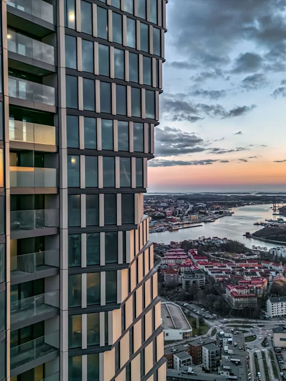 Modern byggnadsfasad som speglar en levande solnedgång över en stad med flod och broar.