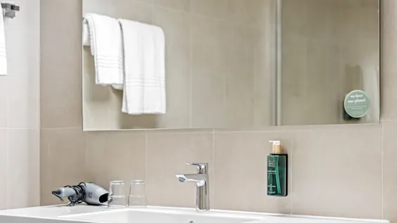 A modern bathroom sink with a hairdryer, two glasses, and a bottle of handwash, reflecting the conservation message on the mirror: "we love our planet".
