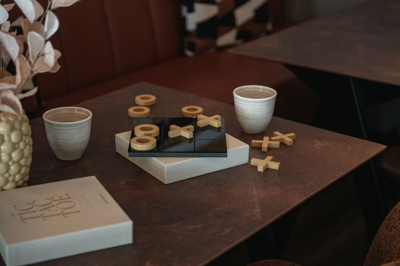 En koselig scene med et tripp-trapp-tresko-spill på et bord, sammen med to kopper og en dekorativ vase. Spilleesken sier TIC TAC TOE.