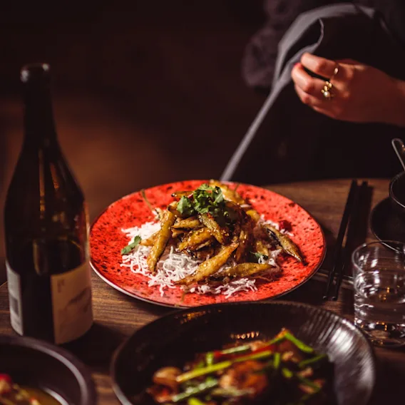 A person enjoying a meal at a restaurant, with a variety of dishes and drinks on a wooden table.