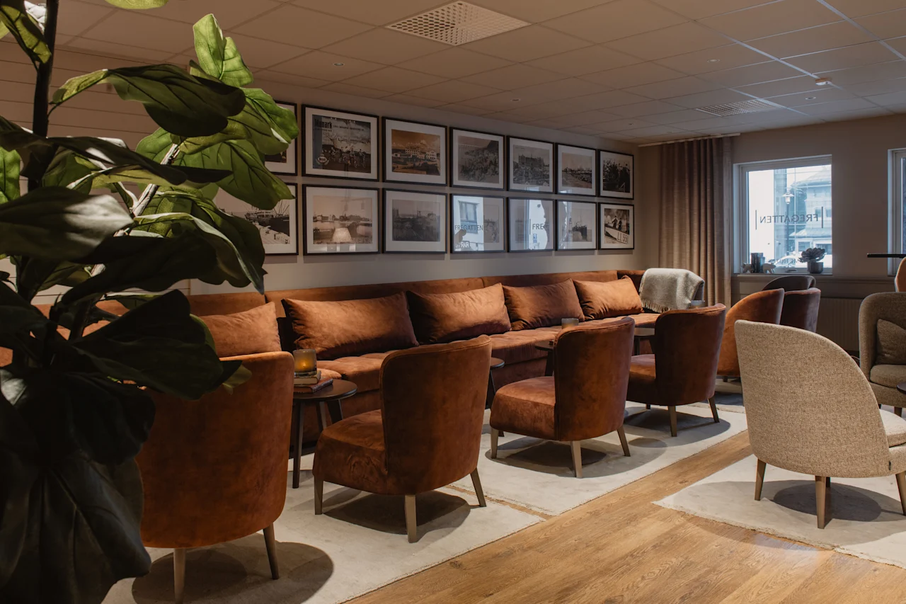 Et varmt og indbydende loungeområde med komfortable siddepladser, indrammet kunst på væggen og en stor grøn plante. Synlig tekst: FREE TERRAZZI.