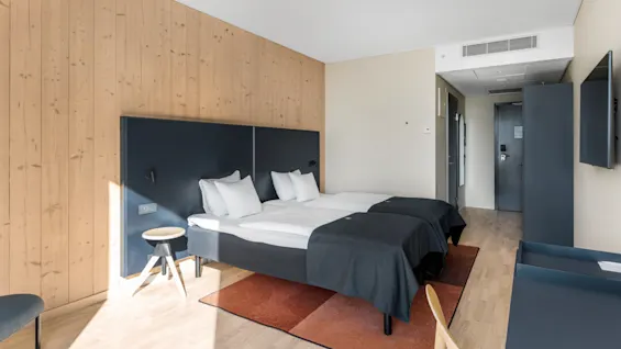 Et moderne hotelværelse med to enkeltsenge, en træpanelvæg og et skrivebordsområde, designet for komfort og funktionalitet.