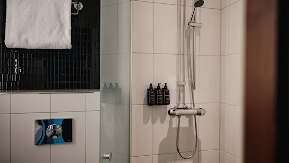 Ett modernt hotellbadrum med duschutrymme, vita och svarta kakelplattor, en dusch och toalettartiklar, redo att användas.