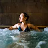 En kvinna avslappnar sig i en bubblig jacuzzi, blickar lugnt åt sidan i en kaklad spa-liknande miljö.