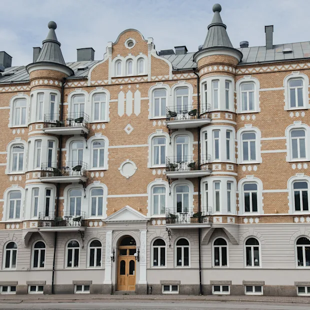 En rikt utsmyckad fyravåningsbyggnad med rundade torn och flera fönster visar en klassisk arkitektur. Balkonger på varje våning är försedda med räcken, i en stadsmiljö.