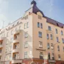 En beige flerbostadsbyggnad med mörkt tak står vid ett gathörn. Skyltar lyder "HOME HOTEL DROTT" och "CARLSTAD ÖLHALL". Balkonger är framträdande på ena sidan.