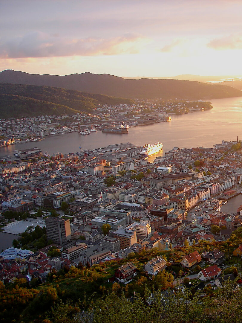 Utsikt från en bergssida över norska staden Bergen i solnedgång.