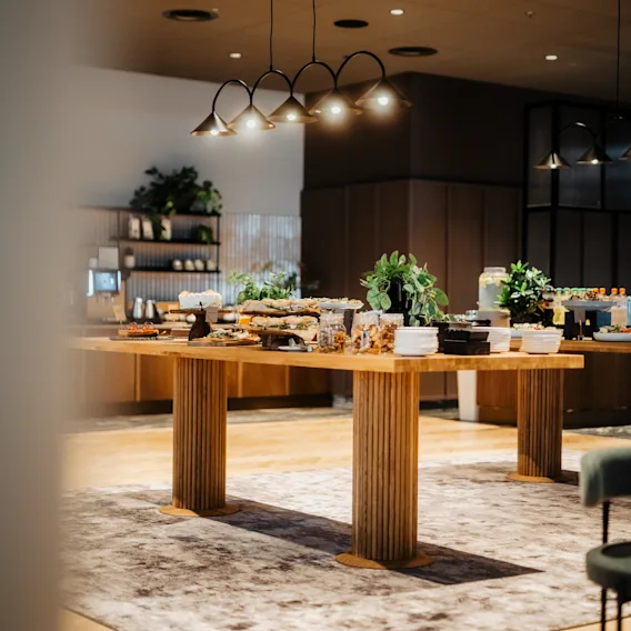 Kauniisti katettu noutopöytä ruokineen ja kasveineen modernin valaistuksen alla. Konferenssi Clarion Hotel Helsinki Airportissa.