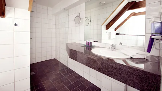 A modern bathroom with a double sink, large mirror, and tiled walls.