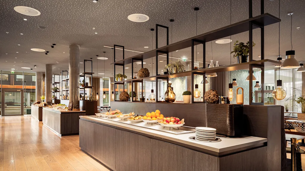Buffetbord med frukt og ulike retter er plassert i et moderne spisestueområde med tregulv og dekorativ belysning.