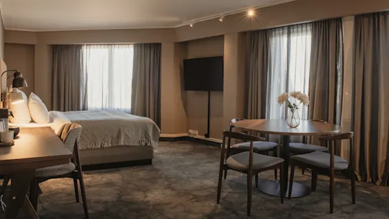 Et moderne hotellrom med en komfortabel seng, en arbeidsplass, en TV og et spiseområde med bord og stoler.