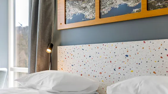 Pillows on a neatly made bed with a terrazzo headboard, map artwork above, and a window with curtains.