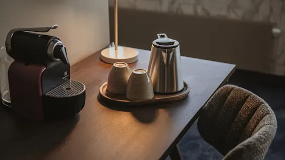 En kaffemaskin, vannkoker og kopper på et brett, klart for en varm drikke.