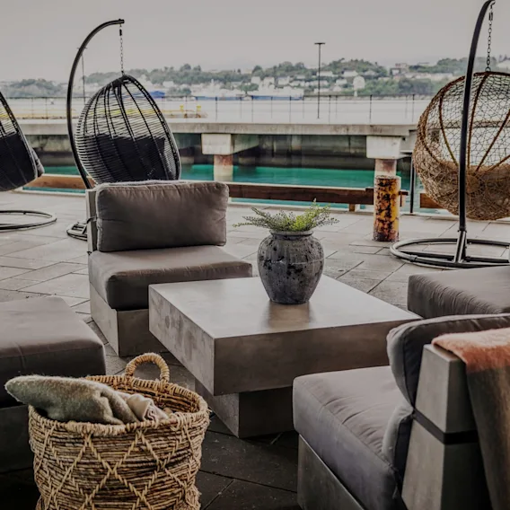 Utendørs hotellounge på terrassen med behagelige lenestoler og hengestoler ved vannet.