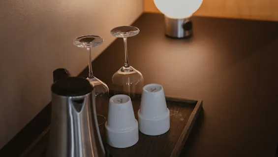 Enjoying a cozy moment at Home Hotel Uppsala with a kettle, wine glasses, and cups on a tray, softly lit by a bedside lamp.