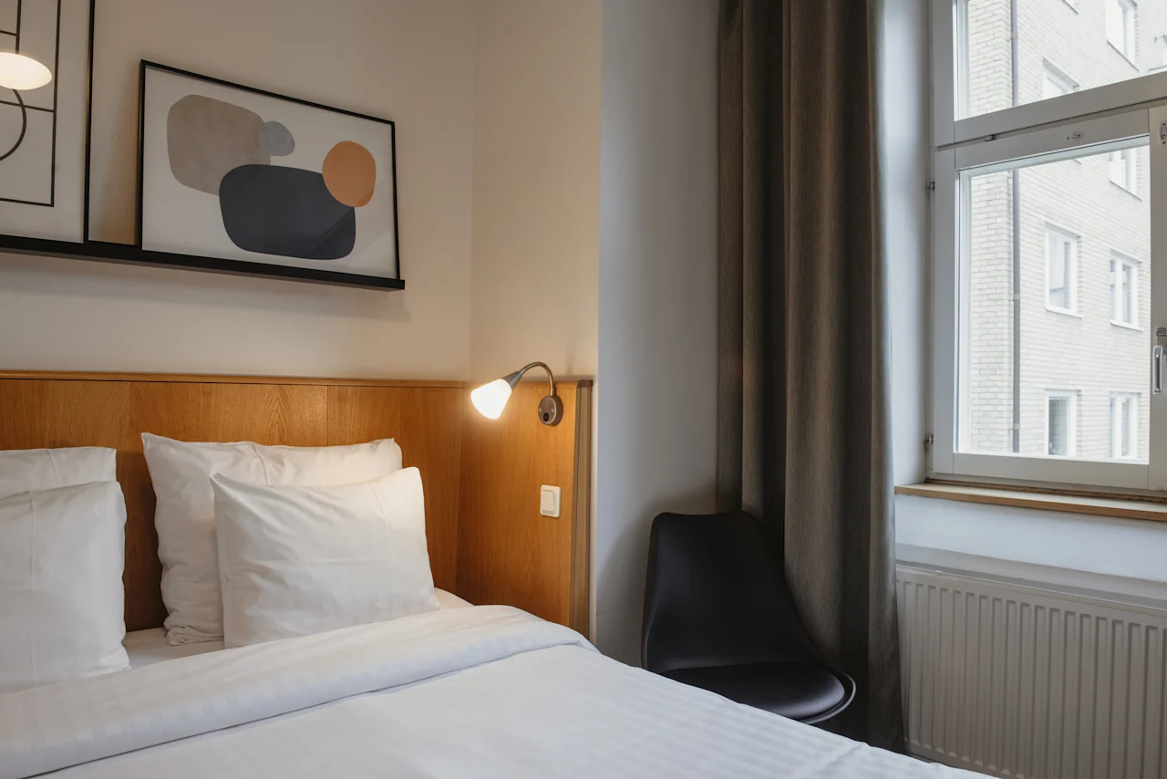 A cozy hotel room with a neatly made bed, a modern lamp, and abstract art on the wall. Home Hotel Uppsala.