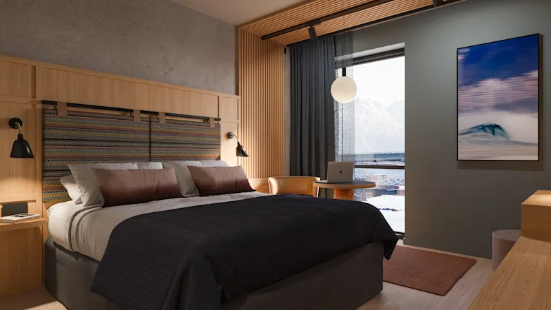 Et moderne hotelværelse med komfortabel seng, bærbar computer på bord og stor vinduesudsigt over sneklædte bjerge.