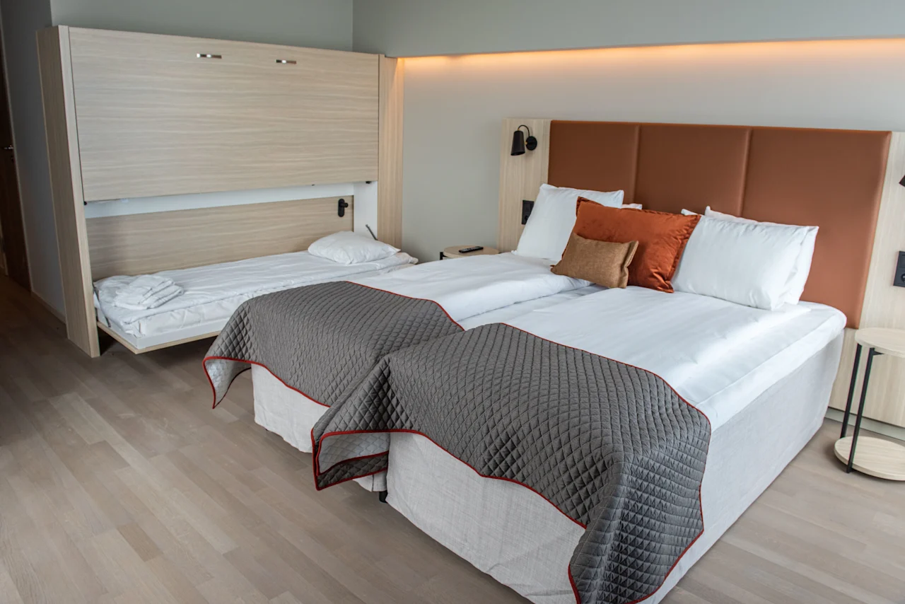 Et moderne hotellrom med to komfortable senger og en ekstra nedfellbar seng, som tilbyr fleksible sovemuligheter.