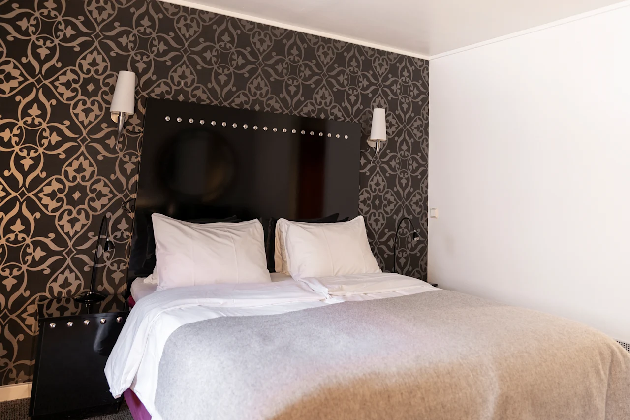 Viihtyisä makuuhuone, jossa on suuri sänky, kuviollinen tapetti ja pehmeä valaistus, täydellinen rentoutumiseen.