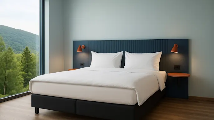 A modern hotel room with a comfortable bed, bedside lamps, and a large window offering a serene view of a lush green forest.