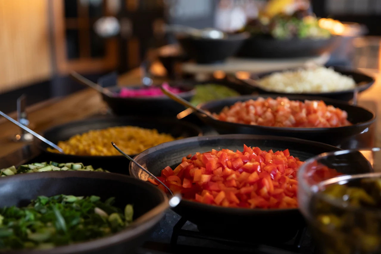 Et farverigt buffetbord med et udvalg af friske, hakkede grøntsager og tilbehør i forskellige skåle, klar til udvælgelse.